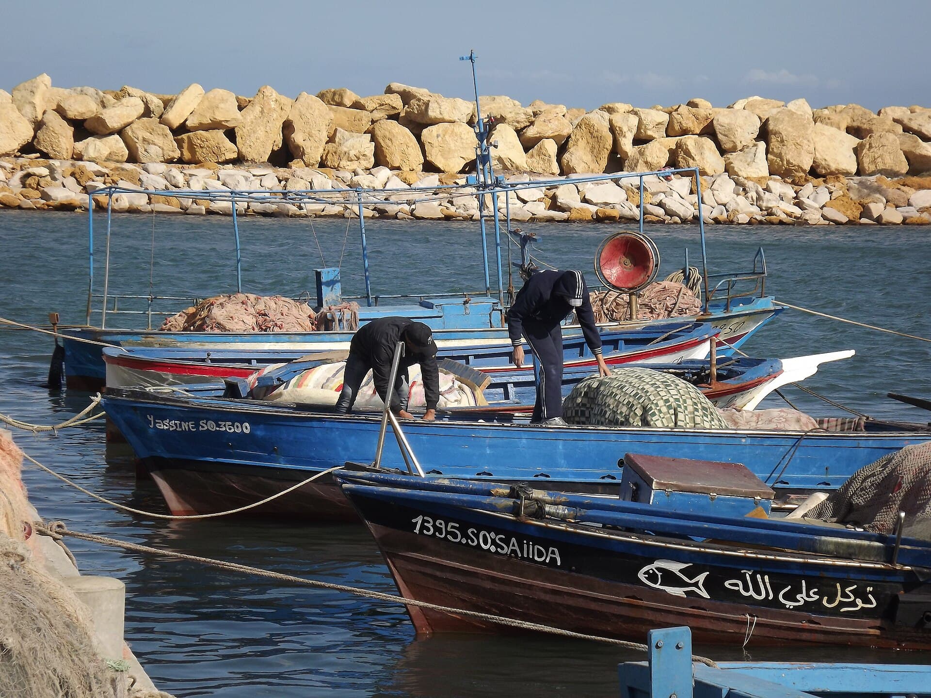 Pêcheurs penchés sur leurs barques bleues au petit port de pêche