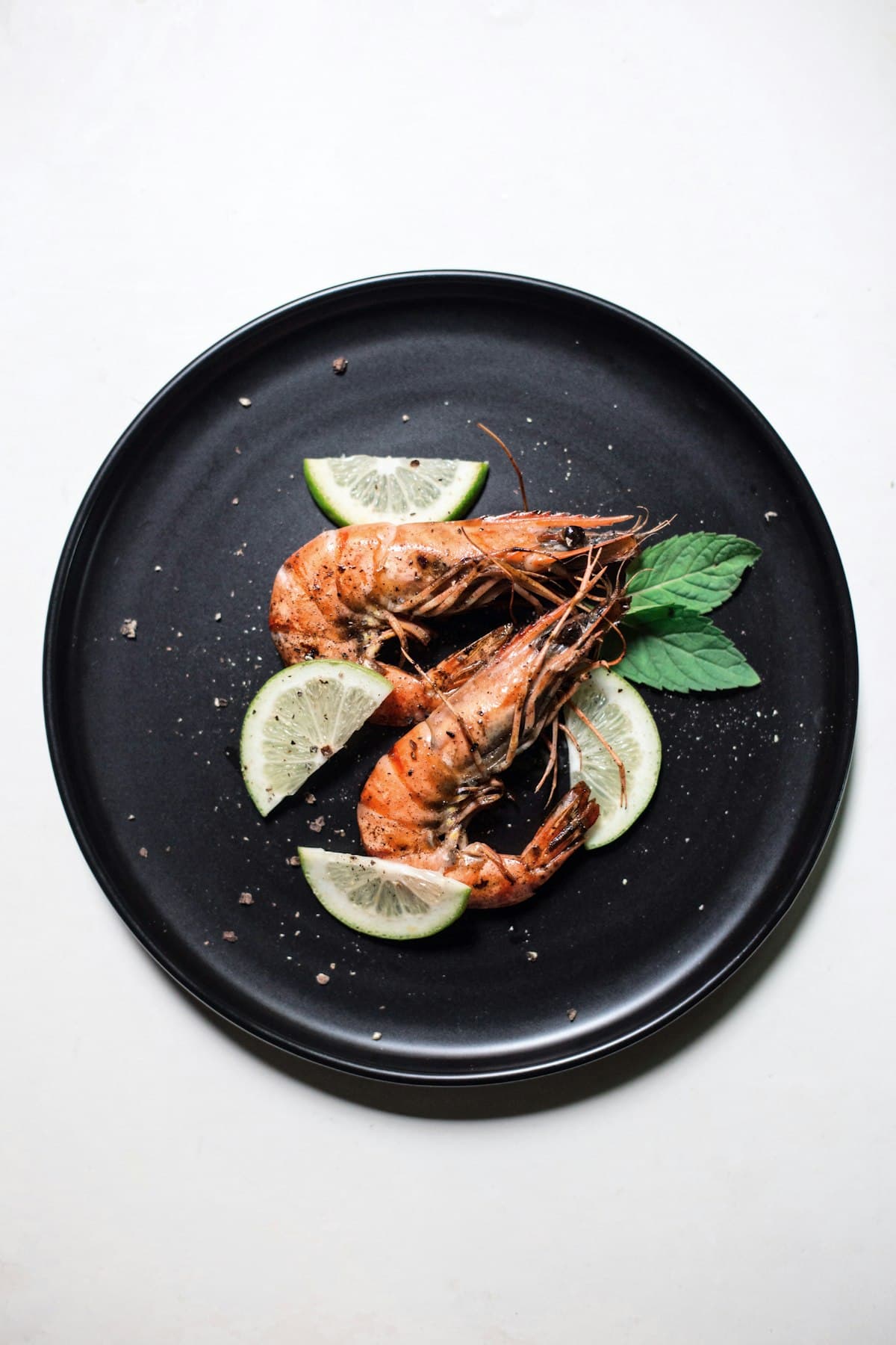 Gambas entières grillées, quartiers de citron vert et menthe sur assiette noire
