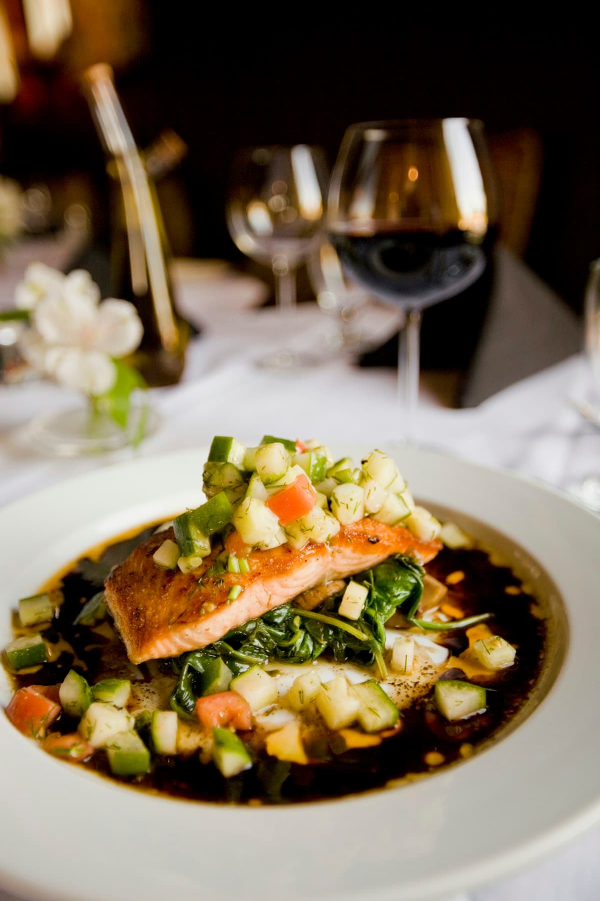 Filet de poisson sauvage dressé sur légumes glacés, verre de vin en arrière-plan