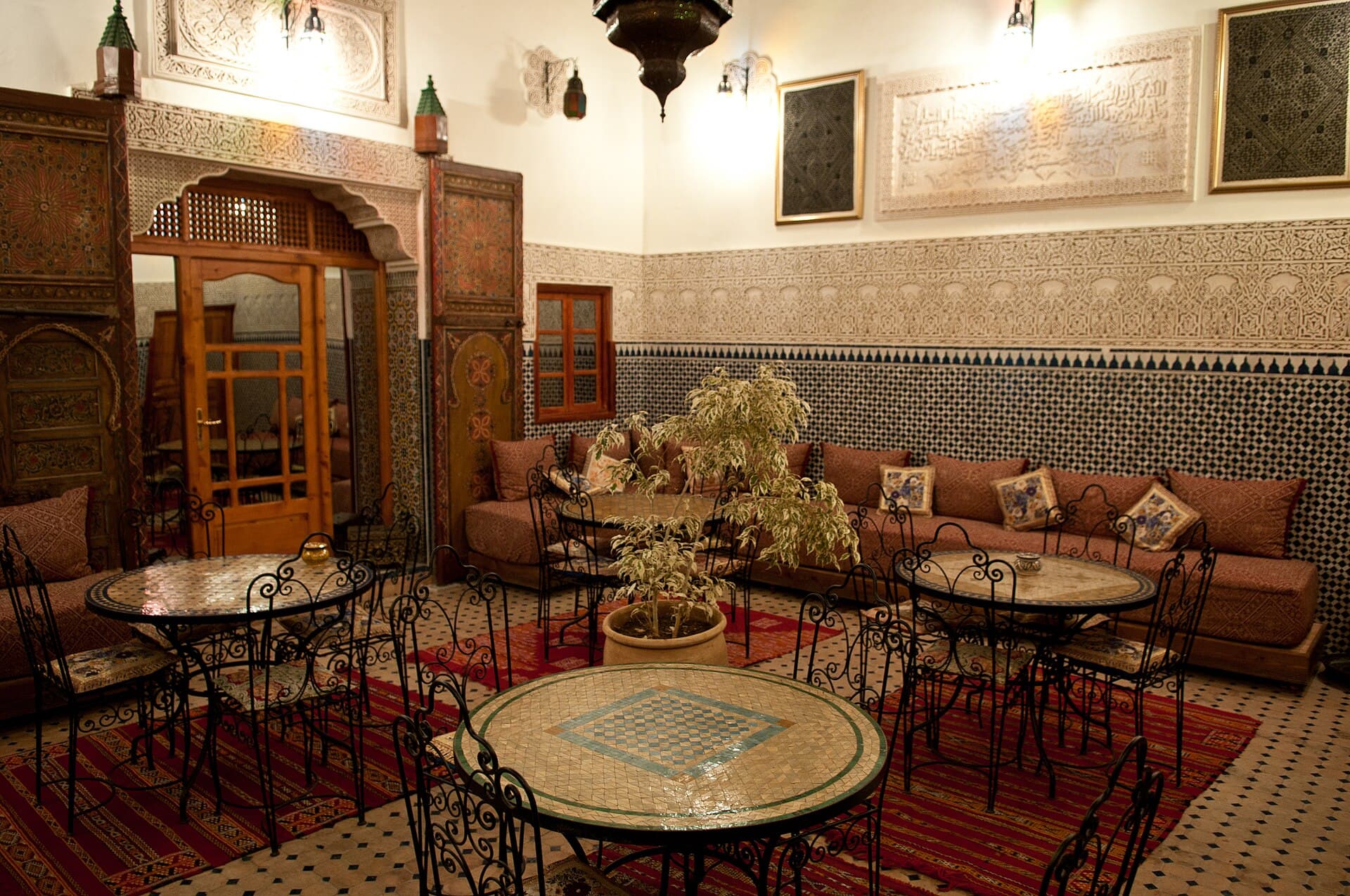 Patio couvert aux murs ouvragés, tables en mosaïque et lanternes du soir