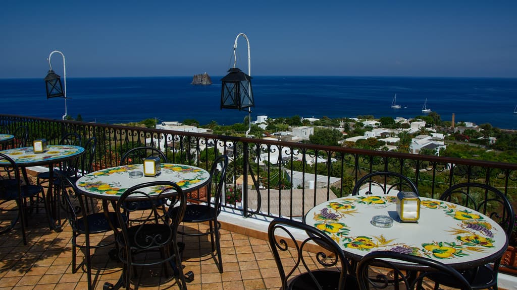 Terrasse dressée face à la mer, lanternes en fer forgé et nappes au vent